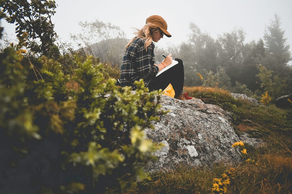 mulher na natureza a escrever num caderno em momento de reflexão e desenvolvimento da autoestima na vida adulta
