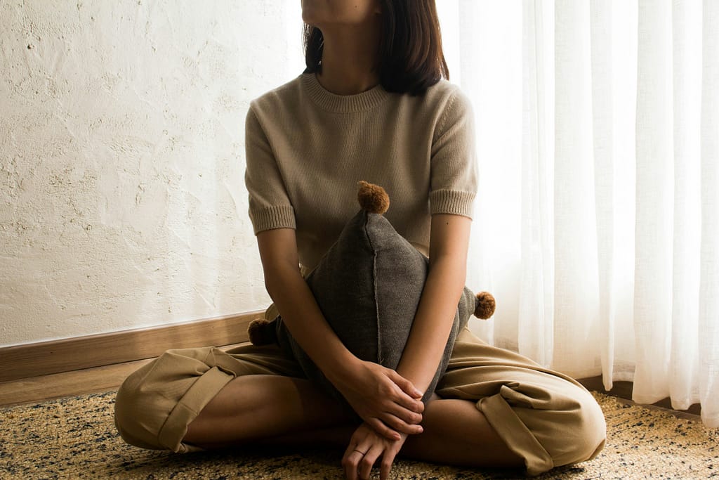 Pessoa sentada no chão com uma almofada, num ambiente calmo, representando tristeza persistente e mal-estar emocional.